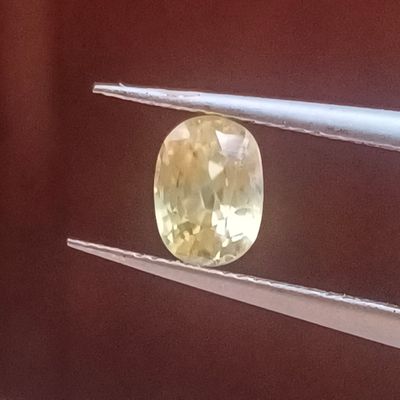 un diamant jaune de forme ovale est maintenu par une paire de pinces