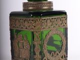 a green glass jar with a gold decoration on it