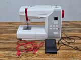 a white sewing machine on a wooden table with a red cord
