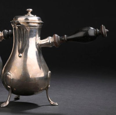 une cafetière en argent posée sur un support, sur fond noir