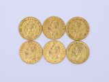 six gold sovereigns of various sizes and shapes on a white surface