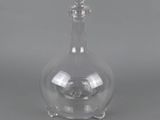 une carafe en verre transparent avec un socle en métal, sur fond gris
