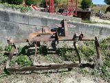 une charrue rouillée posée dans l'herbe, près d'un mur de briques