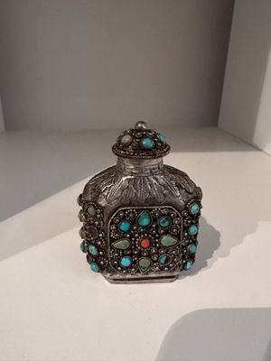 a silver and turquoise glass perfume bottle sitting on top of a white table