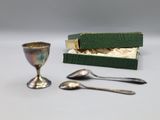 a small silver cup and spoon sitting next to a green box