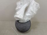 a black vase with plastic wrap on it next to a needle