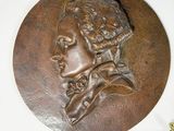 three bronze medallions on a white surface with one of them being a woman