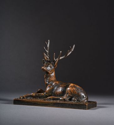 une sculpture en bronze représentant un cerf posé sur un socle en bois