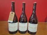 trois bouteilles de vin sont posées sur une table, accompagnées d'une étiquette de prix