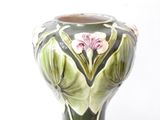 a green vase with pink flowers on it on a white surface