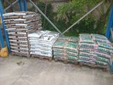 many bags of cement sitting on pallets in front of a fence