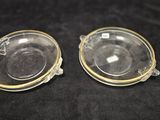 two clear glass dishes with gold rims on a black surface