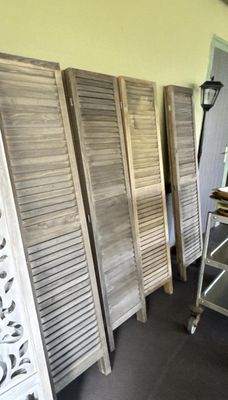 Plusieurs volets en bois sont alignés contre un mur dans une pièce