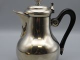 a silver coffee pot with a black handle on a grey surface