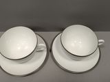 two white cups and saucers sitting on top of a table
