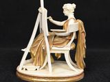 an image of a figurine of a woman sitting at a easel