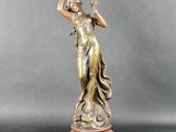 une statue antique en bronze représentant une femme tenant une fleur à la main