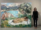 une femme debout devant un tableau représentant une femme allongée sur une serviette