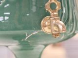 a green vase with a gold handle on a table