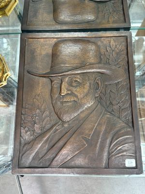 une plaque en bronze représentant un homme coiffé d'un chapeau, posée sur une table en verre