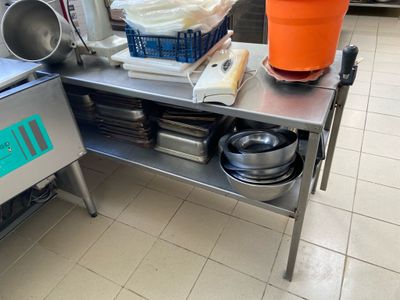 table en acier inoxydable sur laquelle sont posés des casseroles et des poêles, dans une cuisine professionnelle