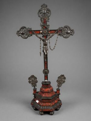 a silver and red cross on a stand with a chain around it