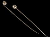 a pair of metal needles with pearls on them against a black background