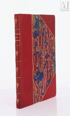 an old book with a red cover and gold trim on a white surface