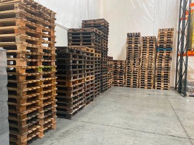 de nombreuses palettes de bois empilées au sol dans un entrepôt