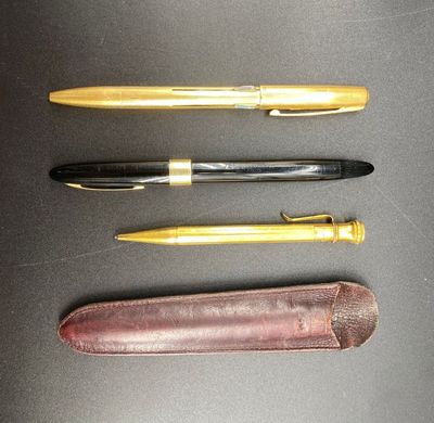 three pens are lined up on a black surface with a leather case