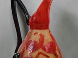 a red and yellow vase with a black handle on a table