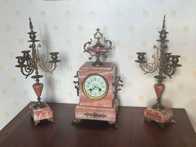trois horloges posées sur une table sur laquelle se trouvent trois bougies
