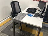 a desk with two computers and a chair in the corner