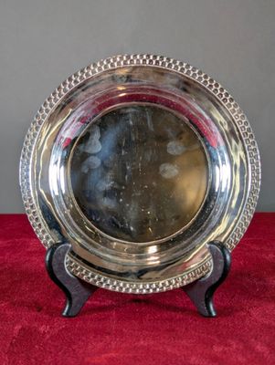 un plat ancien en argent posé sur un socle, sur un tapis rouge