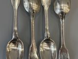 five silver spoons are lined up against a gray wall