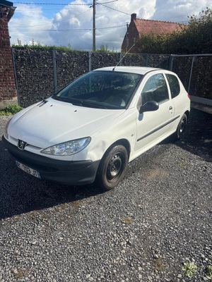 La voiture blanche est garée sur le parking, à côté d'une clôture.