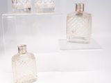 three clear glass bottles with silver lids on display on a white surface