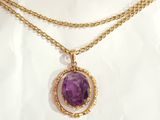 a close up of a necklace with a purple stone on a gold chain