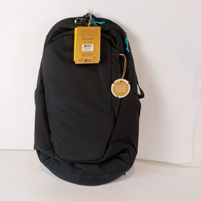 un sac à dos noir muni d'une étiquette, posé contre un mur