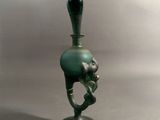 a green glass vase with a black handle on a stand