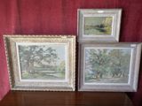 trois tableaux encadrés représentant des arbres et une rivière sont posés sur une table