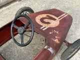 a small red pedal car with a dollar sign on the steering wheel