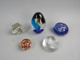 Plusieurs objets en verre de différentes couleurs sont posés sur une surface blanche.