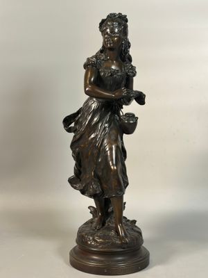 une statue antique en bronze représentant une femme tenant un panier de fleurs