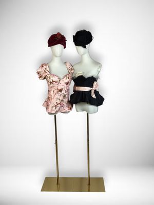 two mannequins dressed in black and pink dresses stand on a gold stand
