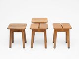 trois petits tabourets en bois placés les uns à côté des autres sur une surface blanche