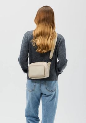 the back view of a woman wearing a grey sweater and jeans with a white cross body bag