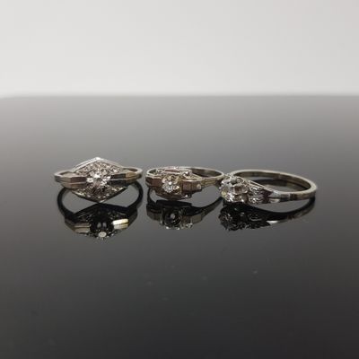 trois bagues en diamant posées sur une surface noire, sur fond blanc