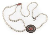 a close up of a necklace with pearls and a red stone