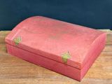 an old red box sitting on top of a wooden table next to a black wall